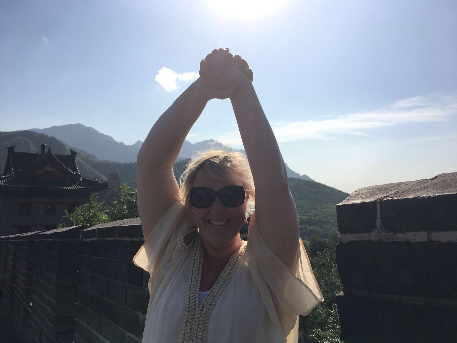 Sacha on the Great Wall of China, arms raised, holding her own hands above her head, smiling